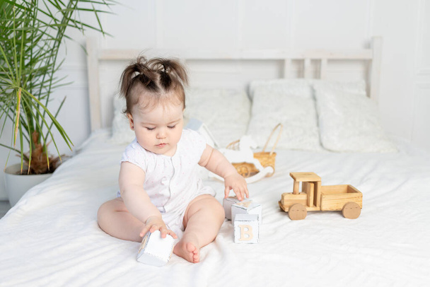 Baby Mädchen spielt mit Holzwürfeln auf dem Bett zu Hause in einem hellen Raum, das Konzept der frühkindlichen Entwicklung - Foto, Bild