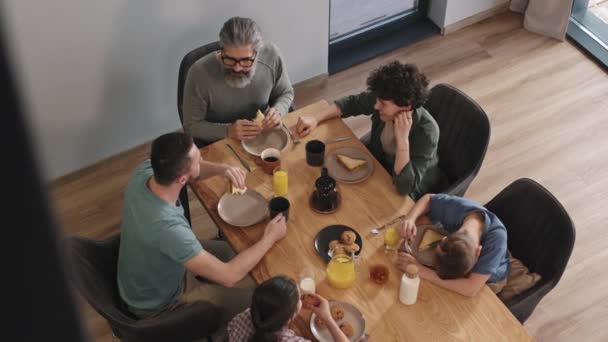 Slowmo top view πλάνο της σύγχρονης καυκάσιας οικογένειας που αποτελείται από δύο παιδιά, γονείς και ο παππούς κάθεται στο τραπέζι της κουζίνας έχοντας πρωινό μαζί και αφήγηση ειδήσεων - Πλάνα, βίντεο