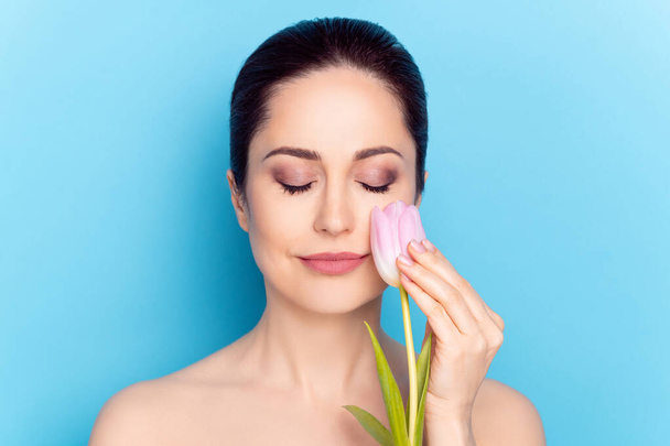 Portrait of attractive trendy calm peaceful nude woman touching cheek tulip cosmetic isolated over bright blue color background - Фото, зображення