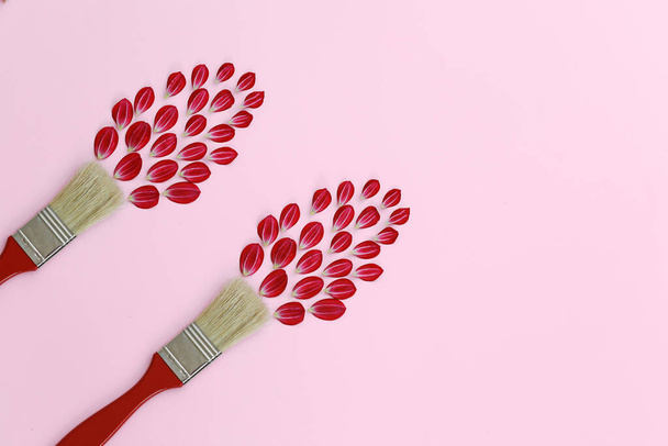 Kreatives Layout mit Pinsel und roten Blütenblättern auf rosa Hintergrund. Pinselfarben mit Blumen. Kopierraum, flache Lage, Draufsicht. - Foto, Bild