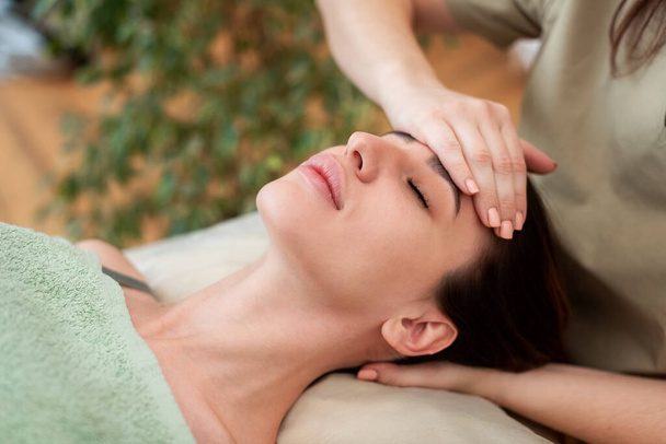 Face of the girl close-up, the massage therapist makes massage. Green background - Φωτογραφία, εικόνα