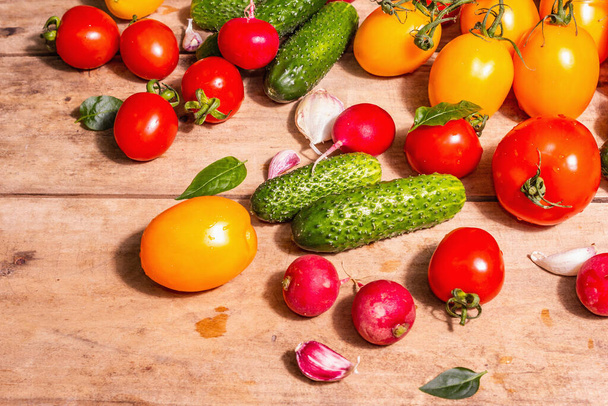 Ruokaa, sadonkorjuuta, kesäkonseptia. Valikoima kypsiä luomuviljelijöitä punaisia ja keltaisia tomaatteja, kurkkuja, retiisiä, valkosipulia ja tuoreita basilikaa. Vanha puinen pöytä, paikka tekstin - Valokuva, kuva