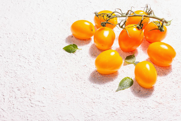 Yellow-orange tomatoes on light plaster background. Fresh ripe vegetables, harvesting concept. A trendy hard light, dark shadow, copy space - Photo, Image