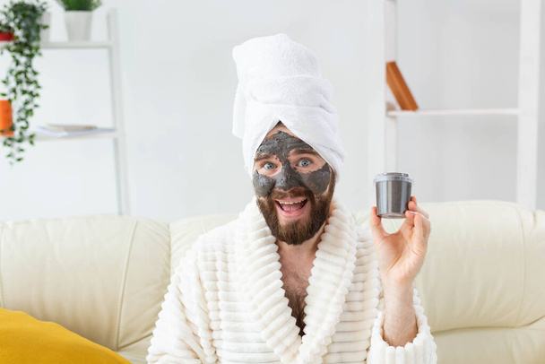 Brodatego mężczyznę bawiącego się maską kosmetyczną na twarzy zrobioną z czarnej gliny. Mężczyźni pielęgnacja skóry, humor i spa w domu koncepcja - Zdjęcie, obraz