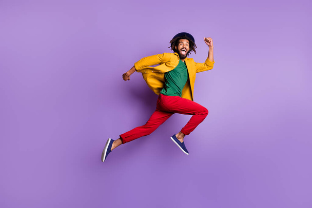 Full length photo of cute dark skin man wear yellow shirt cap jumping high running isolated violet color background - Photo, image