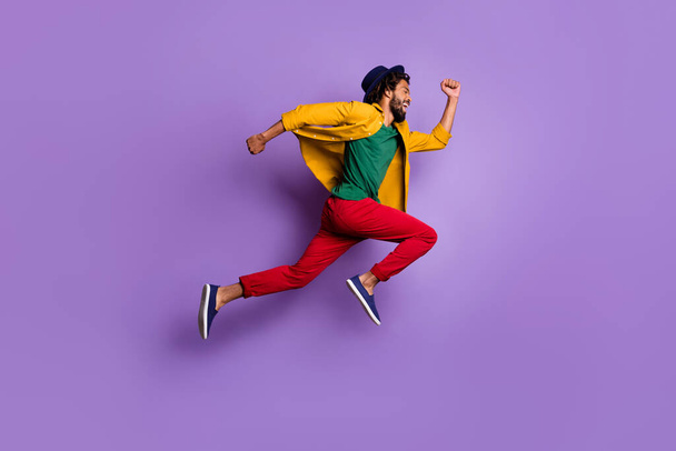 Full length photo of purposeful dark skin guy dressed yellow shirt headwear jumping running fast isolated purple color background - Photo, Image