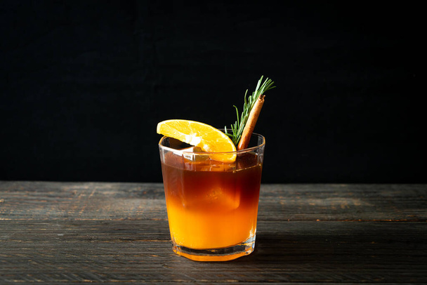 A glass of iced americano black coffee and layer of orange and lemon juice decorated with rosemary and cinnamon - Foto, imagen