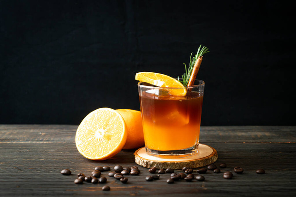 A glass of iced americano black coffee and layer of orange and lemon juice decorated with rosemary and cinnamon - Foto, Imagem