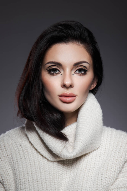 Beauty portrait of woman in white sweater, perfect evening makeup on dark background. Perfect skin without wrinkles, professional beauty makeup, long black hair - Foto, immagini