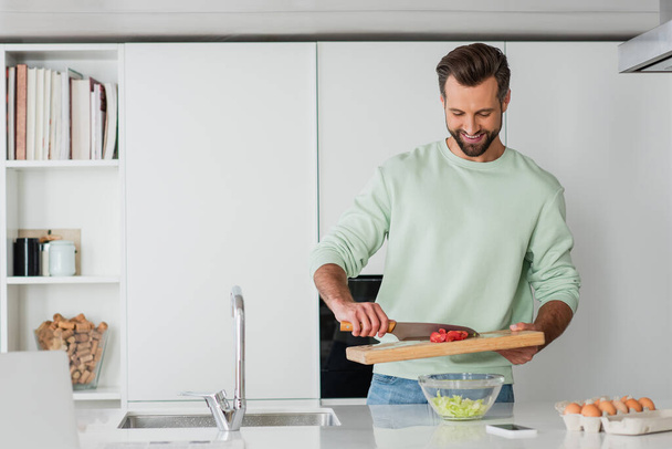 positive man smiling while cooking breakfast in kitchen - Φωτογραφία, εικόνα