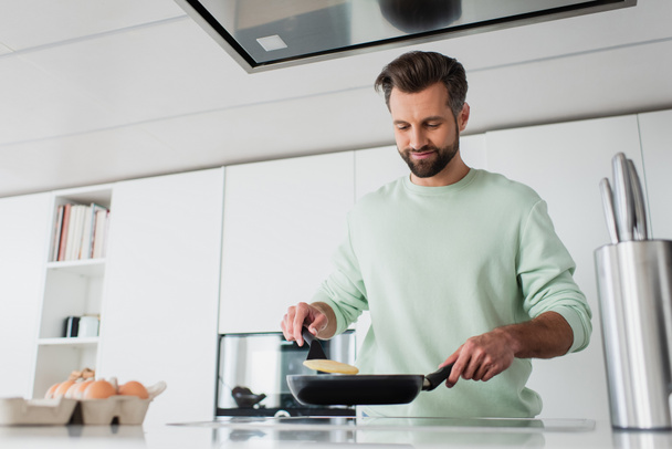 pleased man preparing pancakes for breakfast in kitchen - Фото, зображення