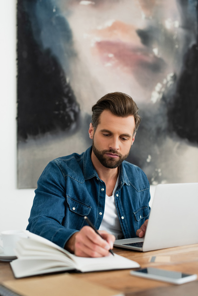 man in denim shirt writing in notebook while working at home - Φωτογραφία, εικόνα
