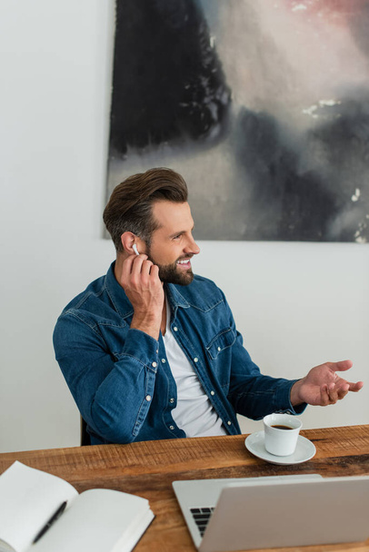 happy freelancer adjusting earphone while sitting at workplace - Фото, зображення