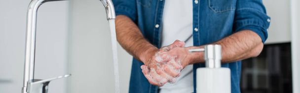 przycięty widok człowieka mycie rąk w pobliżu zamazanego pojemnika z mydłem, baner - Zdjęcie, obraz