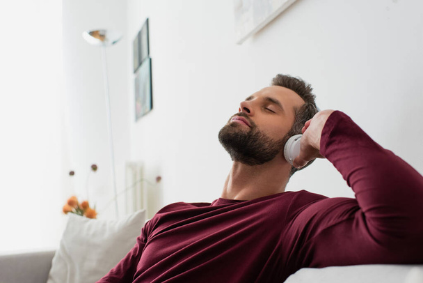 relaxing man listening music in wireless headphones with closed eyes - Zdjęcie, obraz