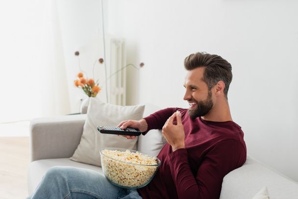 смеющийся человек ест попкорн во время просмотра комедийного фильма в гостиной - Фото, изображение
