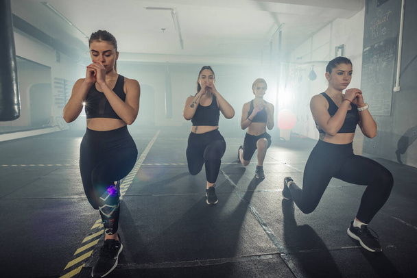 Spor kıyafetli bir grup kadın spor salonunda sol bacağıyla atlama egzersizi yapıyor. - Fotoğraf, Görsel