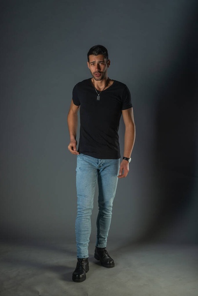 Sexy young man wearing a black t-shirt and jeans poses on isolated black background - Foto, Bild
