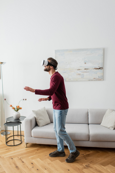full length view of adult man in vr headset gaming in living room - Photo, Image