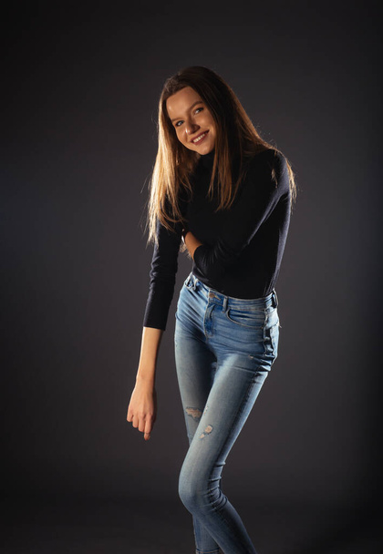 A fashionable young woman in black roll neck posing isolated on a dark background - Photo, Image
