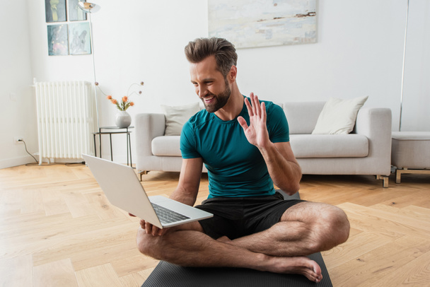 hombre feliz tener videollamada en el ordenador portátil mientras practica yoga en casa - Foto, imagen