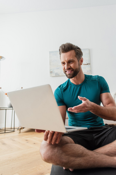 hymyilevä mies osoittaa laptop istuessaan lootus aiheuttaa jooga matto - Valokuva, kuva