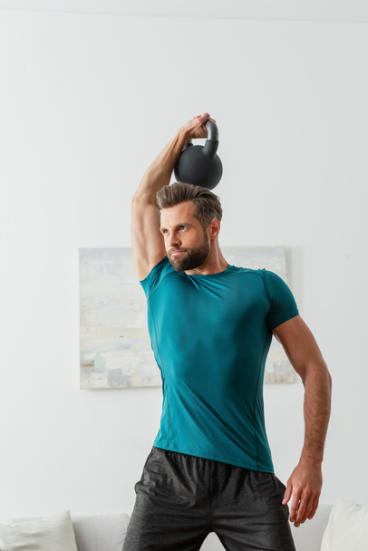 athletic man in sportswear working out with kettlebells at home - Фото, зображення