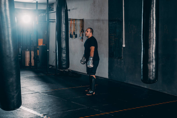 Atraktivní mladý muž trénink vedle boxovací pytel a nošení boxerských rukavic - Fotografie, Obrázek