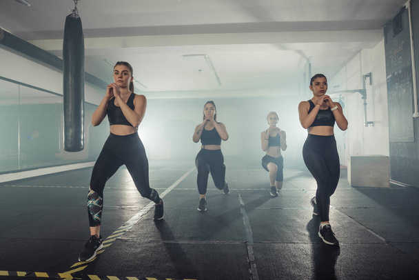 Gruppe von Sportlerinnen in Sportbekleidung bei Ausfallgymnastik im Fitnessstudio mit dem rechten Bein - Foto, Bild