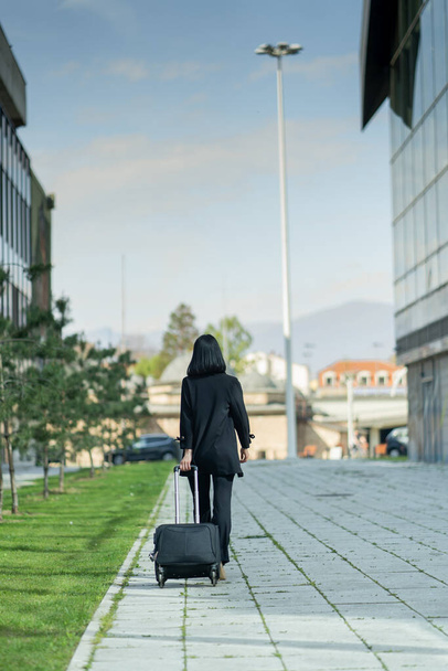 Attractive businesswoman is walking away from the company with her traveling bag - 写真・画像