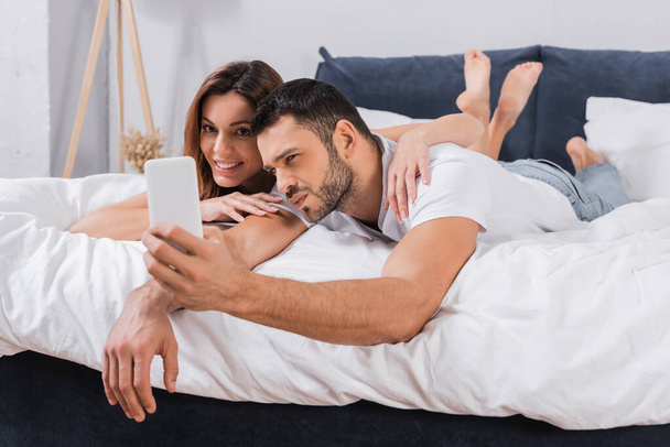 Smiling woman embracing boyfriend during selfie in bedroom  - Фото, зображення