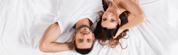 Top view of young couple looking at camera on bed, banner  - Foto, afbeelding