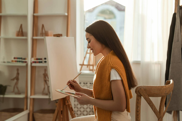 Beautiful young woman drawing on easel at home - Fotoğraf, Görsel
