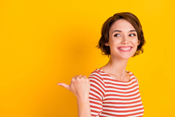 Photo of attractive person in good mood watch empty space point thumb isolated on yellow color background - Zdjęcie, obraz