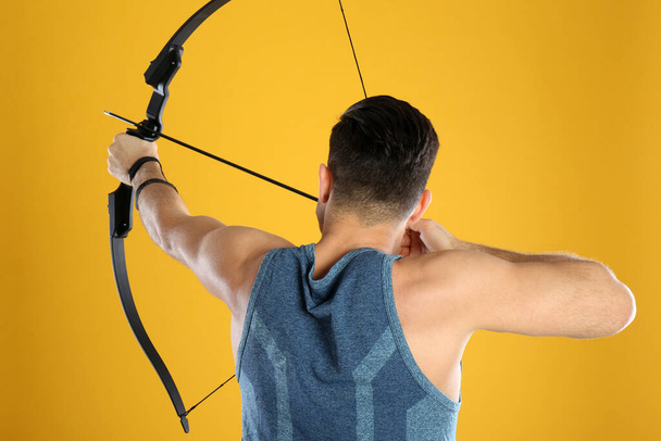 Man with bow and arrow practicing archery on yellow background, back view - Foto, immagini