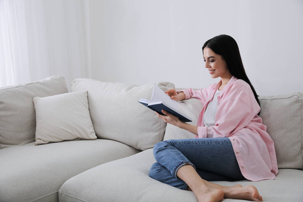 Woman reading book on sofa in living room - Foto, imagen