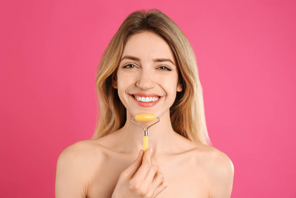 Young woman using natural jade face roller on pink background - Φωτογραφία, εικόνα