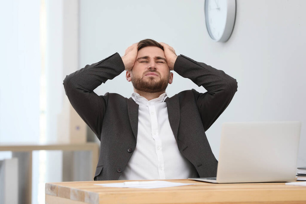 Man suffering from migraine at workplace in office - Фото, изображение