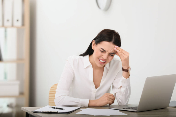 Woman suffering from migraine at workplace in office, space for text - Foto, afbeelding
