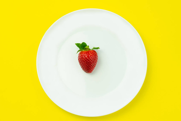 Λευκό πιάτο με μία φράουλα σε απομονωμένο κίτρινο φόντο.Δημιουργική minimal έννοια τροφίμων με χώρο αντιγραφής. - Φωτογραφία, εικόνα