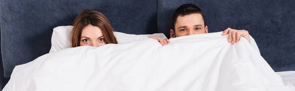 Молода пара покриває обличчя ковдрою на ліжку, банер
  - Фото, зображення