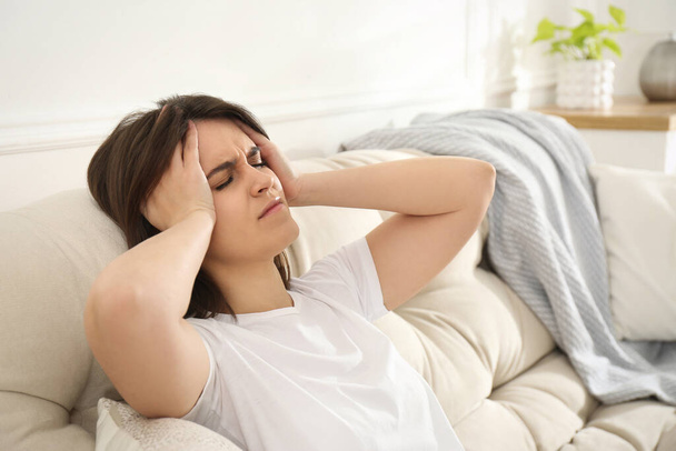 Young woman suffering from migraine on sofa at home - Foto, Imagem