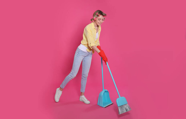 Young housewife with broom and dustpan on pink background - Fotografie, Obrázek