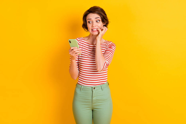 Photo of attractive person bite nail look phone very bad post isolated on vivid yellow color background - Foto, afbeelding