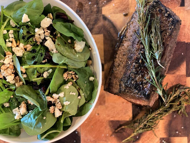 Vleessteak met rozemarijn en spinazie salade met bosbessen en blauwe kaas op houten plank - Foto, afbeelding