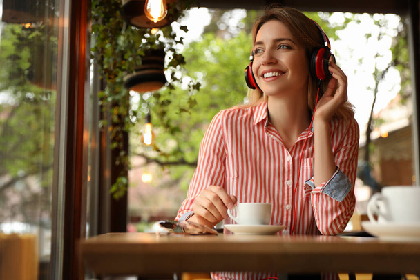 Young woman with headphones listening to music in cafe - Фото, изображение