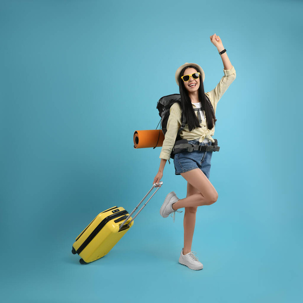 Happy female tourist with backpack and suitcase on light blue background - Valokuva, kuva