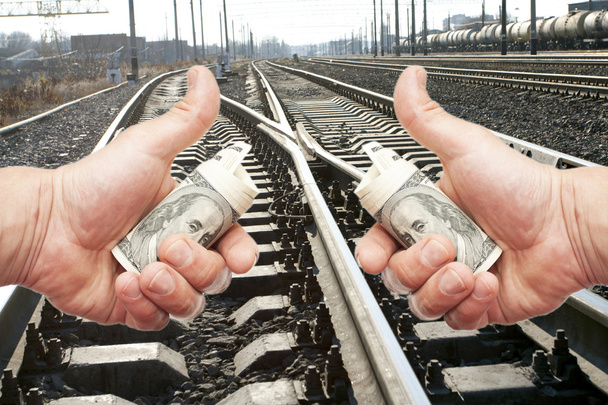 Mãos com notas de dólares contra a via férrea
 - Foto, Imagem