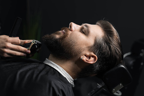 Recortar la barba con una máquina de afeitar. Publicidad para peluquería y salón de belleza para hombres. - Foto, imagen