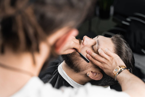 Coupe droite rasoir mans barbe dans le salon de coiffure. Barbier homme faisant coiffure pour bel homme - Photo, image